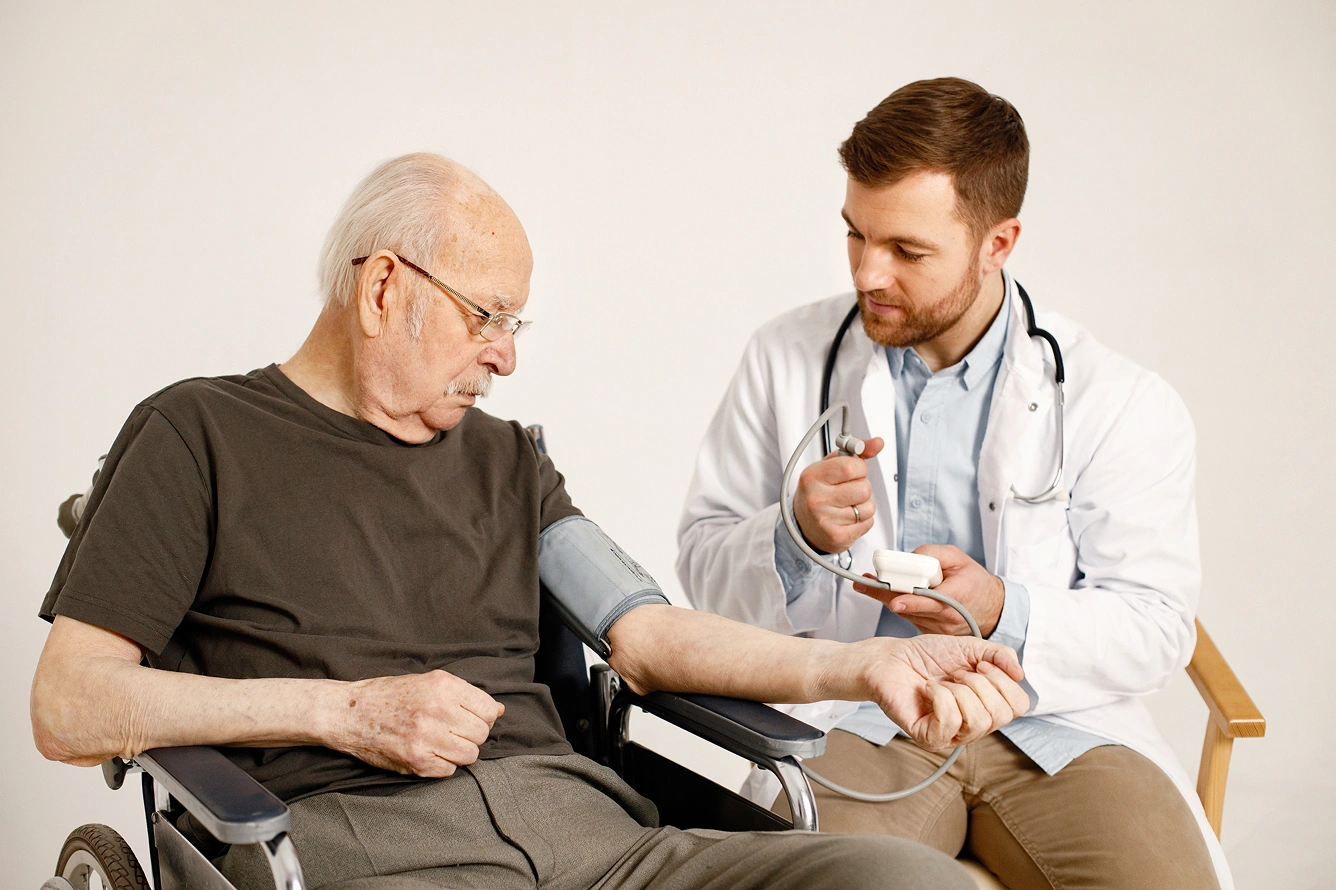 A doctor taking the blood pressure of an elderly male patient seated in a wheelchair, using professional diagnostic medical equipment. A doctor taking the blood pressure of an elderly male patient seated in a wheelchair, using professional diagnostic medical equipment.